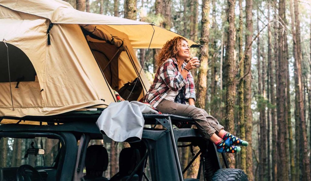 Young Woman Sitting Outside Tent On The Roof Of A Jeep